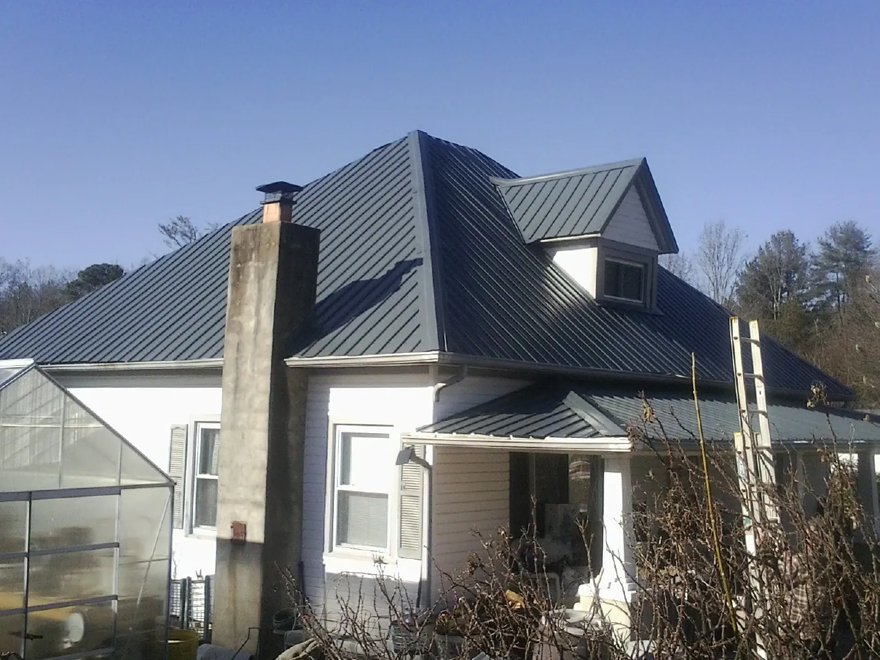 Dark blue standing seam metal roof on a white farmhouse with dormer — Slate & Tile Roof Repair by Roofing Brothers in Virginia City