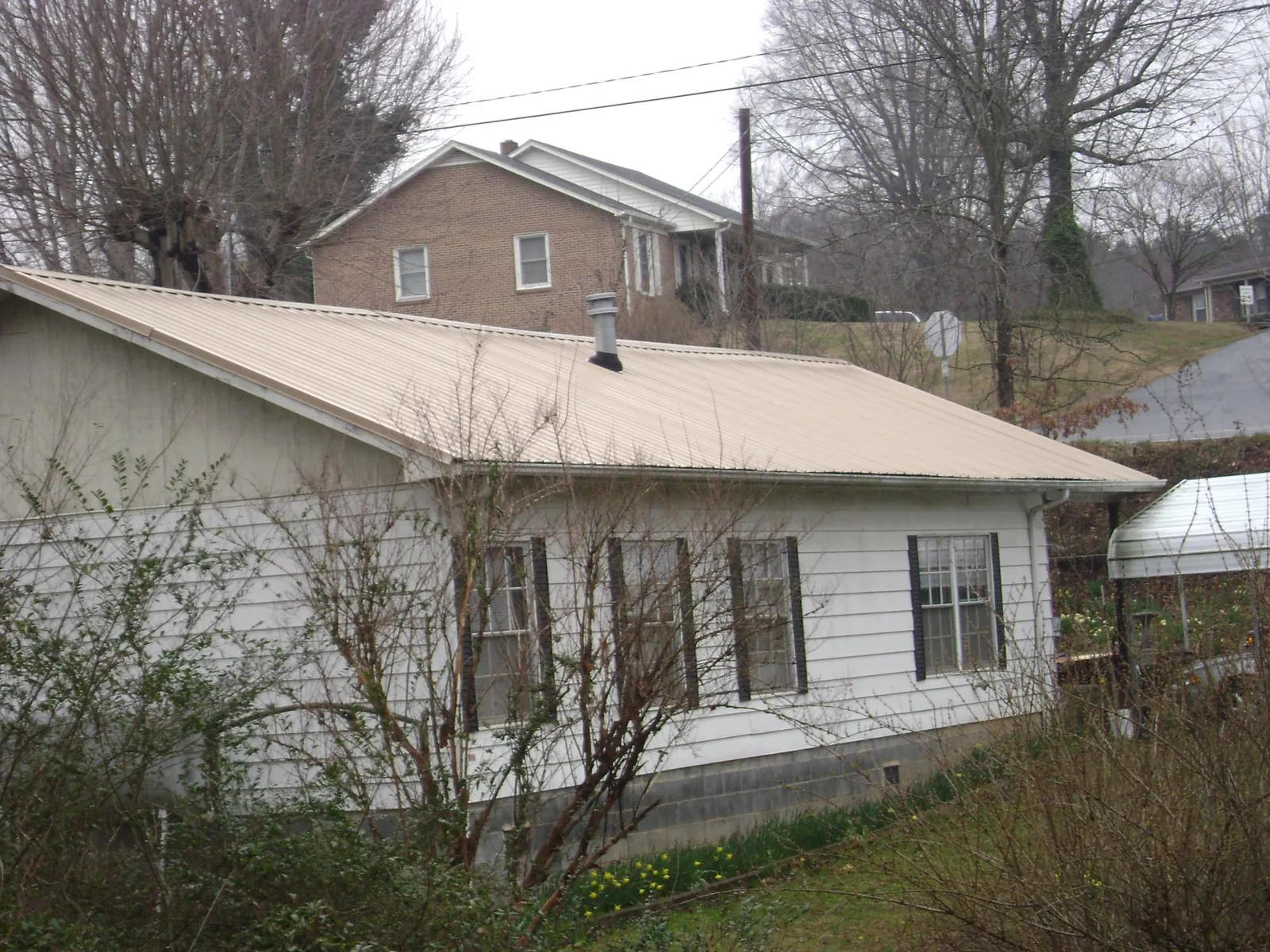 Tan metal roof on a white sided house set into a hillside — Commercial Roofing by Roofing Brothers in Virginia City